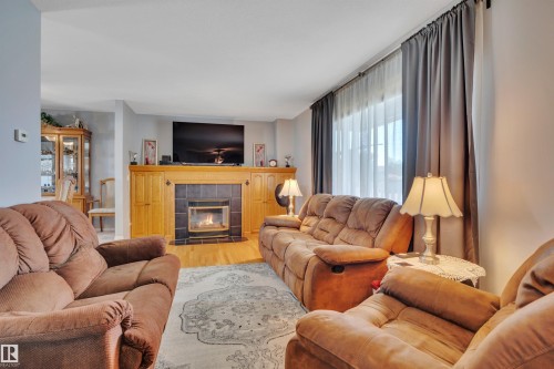Living area featuring a central fireplace with a tile surround and wood mantel, complemented by integrated wood cabinetry - 184 Garwood Cres, Wetaskiwin, AB - Indoor Photo Showing Living Room With Fireplace