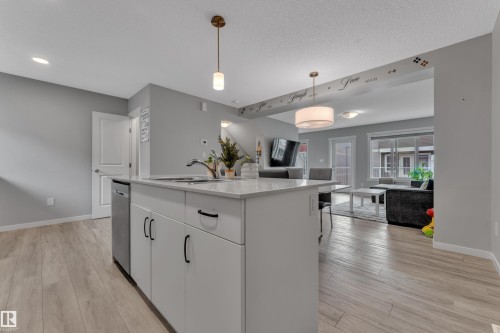 Kitchen island featuring a stainless steel sink, white cabinetry with black hardware, and a light-toned countertop - 82 1816 Rutherford Road, Edmonton, AB 