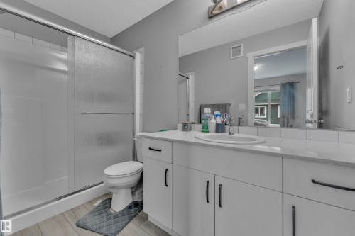Bathroom featuring a single vanity with an integrated sink, a large mirror, and a shower with frosted sliding doors - 82 1816 Rutherford Road, Edmonton, AB 