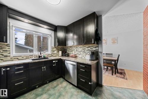 Kitchen featuring dark cabinetry, speckled countertops, and a mosaic tile backsplash - 5418 17A Avenue, Edmonton, AB 