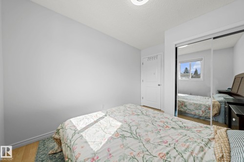 Bedroom featuring light-toned walls, wood-finish flooring, a built-in closet with mirrored sliding doors, and a white paneled door - 5418 17A Avenue, Edmonton, AB 