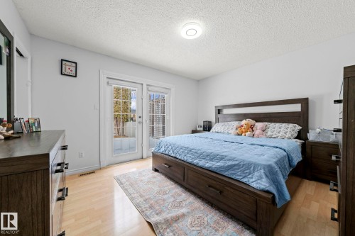 Light-filled bedroom featuring double French doors with exterior access, wood-finish flooring, and a flush-mount ceiling light - 5418 17A Avenue, Edmonton, AB 