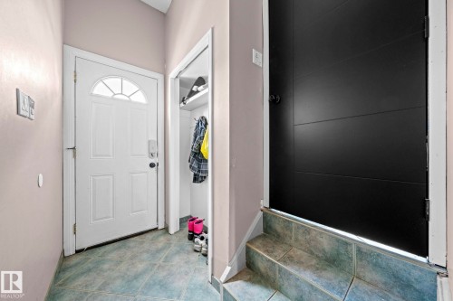 Entryway featuring a white paneled door with a sunburst transom window, a closet with shelving and hanging rod, light gray walls, and green tile flooring - 5418 17A Avenue, Edmonton, AB 