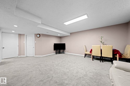 Spacious finished room featuring light gray carpeting, recessed ceiling lighting, a long rectangular flush-mount ceiling light, and neutral-toned wall paint - 5418 17A Avenue, Edmonton, AB 