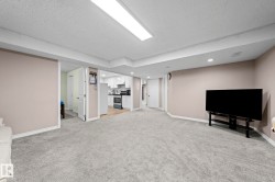 Expansive carpeted area with recessed lighting, complemented by a kitchen space featuring white cabinetry, a built-in oven, and a refrigerator - 