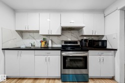 Kitchen featuring white cabinetry, dark countertops, a stainless steel electric range with an overhead vent, a stainless steel sink, and a white marble-patterned backsplash - 