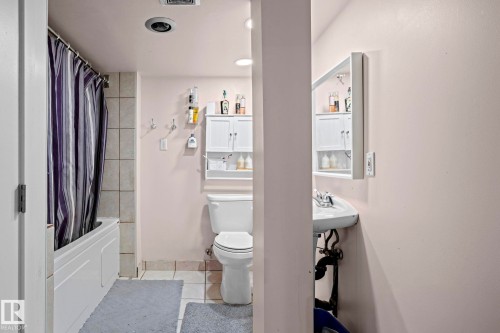 Compact bathroom featuring a white bathtub with tiled surround, a toilet, and a wall-mounted vanity sink with a mirrored medicine cabinet - 5418 17A Avenue, Edmonton, AB 