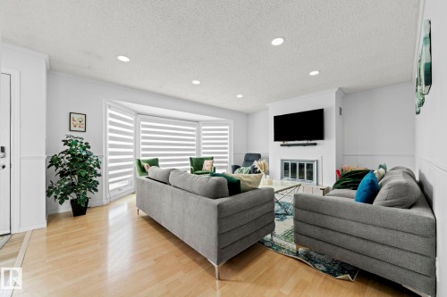 Sunlit living space featuring light wood-finish flooring, recessed lighting, and a prominent bay window with horizontal blinds - 5418 17A Avenue, Edmonton, AB 