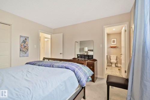 Carpeted bedroom featuring light-colored walls, a textured ceiling, and a doorway leading to an adjoining bathroom with tiled flooring - 10715 33 Avenue, Edmonton, AB 
