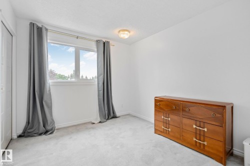 Bright room featuring a large window, light-colored carpeting, white baseboards, and a flush-mount ceiling light fixture - 10715 33 Avenue, Edmonton, AB 