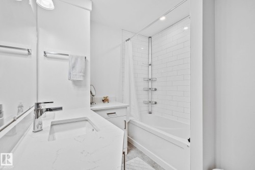 Modern bathroom featuring a built-in tub with white subway tile surround, white integrated sink with chrome faucet, and white countertop with matching cabinetry - 10715 33 Avenue, Edmonton, AB 