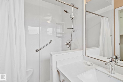 Shower with a built-in grab bar and a handheld showerhead, accompanied by a vanity featuring a white countertop and an integrated sink with a chrome faucet - 10715 33 Avenue, Edmonton, AB 