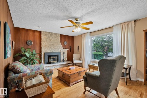 Living area featuring wood-finish flooring, a stone-clad fireplace with a black insert, and wood paneling - 10715 33 Avenue, Edmonton, AB 