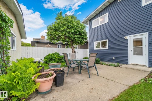 Exterior concrete patio featuring a perimeter of lush green foliage and a mature tree - 10715 33 Avenue, Edmonton, AB 
