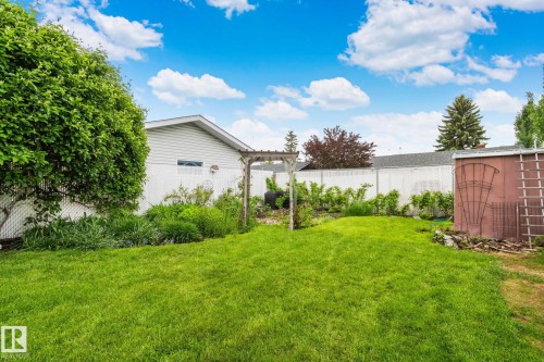 Expansive green lawn with mature perimeter trees and a wooden arbor feature - 10715 33 Avenue, Edmonton, AB 