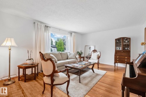 Spacious living area featuring light wood-finish flooring, white walls, and a large window with white drapes - 10715 33 Avenue, Edmonton, AB 