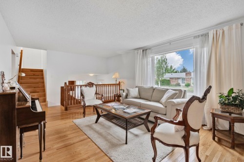 Living area featuring wood-finish flooring, a large picture window, and a wooden staircase with banister - 10715 33 Avenue, Edmonton, AB 