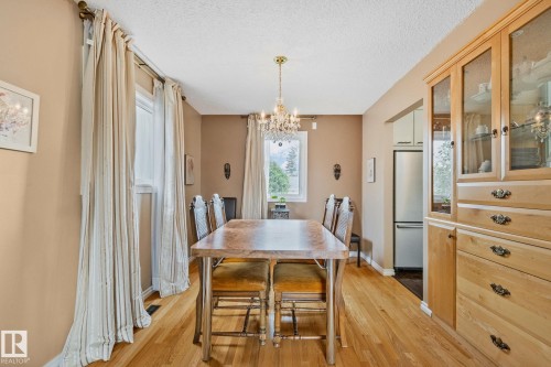 Dining area featuring wood-finish flooring, a brass chandelier, and a built-in wood cabinet with glass door accents - 10715 33 Avenue, Edmonton, AB 