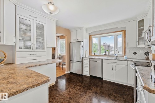Bright kitchen featuring a bay window, white cabinetry, stainless steel appliances, and dark-toned flooring - 10715 33 Avenue, Edmonton, AB 