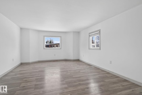 Spacious room featuring light wood-finish flooring, crisp white walls, and two windows with grey trim providing natural illumination - 543 Evergreen Street, Edmonton, AB 