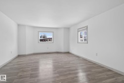 Spacious room featuring light wood-finish flooring, crisp white walls, and two windows with grey trim providing natural illumination - 