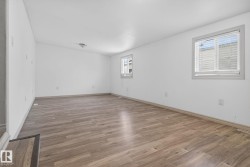 Spacious room featuring wood-finish flooring, white walls, and two windows with blinds - 