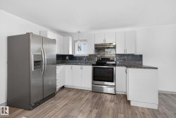 Kitchen featuring wood-finish flooring, white cabinetry, granite-look countertops, and a stone-tile backsplash - 