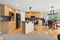 Kitchen featuring wood-finish flooring, light wood cabinetry, stone countertops, a central island with bar seating, and stainless steel appliances - 