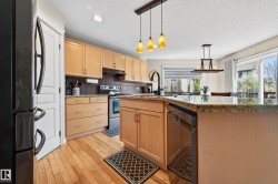 Kitchen featuring light wood cabinetry, granite-finish countertops, stainless steel appliances, and wood-finish flooring - 