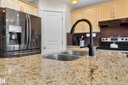 Kitchen featuring a dual basin stainless steel sink with a matte black gooseneck faucet, granite countertops, light wood cabinetry, a stainless steel refrigerator, and a black electric range - 