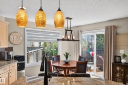 Kitchen and dining area featuring granite countertops, light wood cabinetry, a large window with horizontal blinds, and a sliding glass door to an outdoor deck - 