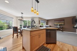 Kitchen island featuring a granite countertop, undermount sink with a matte black faucet, and a stainless steel dishwasher - 