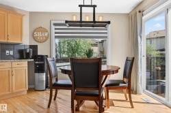 Dining area featuring wood-finish flooring, a contemporary chandelier, and a bright window with horizontal blinds - 
