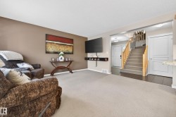 Open-concept living area featuring a neutral carpeted floor, an accent wall, and a stairwell with natural wood handrails - 