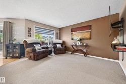 Bright living area featuring light-toned carpeting and a large window with horizontal blinds - 