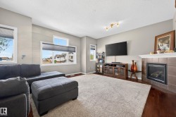 Living area featuring wood-finish flooring, a tiled fireplace with mantel, multiple windows for ample natural light, and track lighting - 