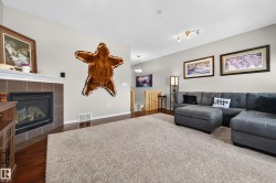 Living area featuring a gas fireplace with a tile surround and white mantel, wood-finish flooring, and a large area rug - 