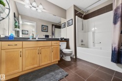 Bathroom featuring a single vanity with light wood cabinetry and a dark countertop, an integrated sink, a large mirror, and a full bathtub with a shower kit - 