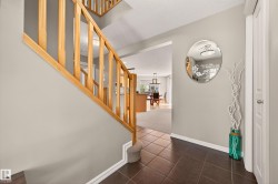 Foyer featuring dark brown tile flooring, light neutral wall paint, and a natural wood staircase with balusters - 