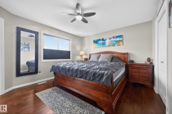 Spacious bedroom featuring dark wood-finish flooring, a large window with privacy blinds, and a ceiling fan with integrated lighting - 