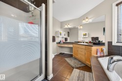 Spacious bathroom featuring a glass-enclosed shower, large vanity with dual sinks, built-in makeup vanity, ample counter space, and a separate soaking tub with chrome fixtures - 