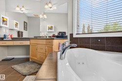 Spacious bathroom featuring a white soaking tub with integrated jets, dual vanity with light wood cabinetry, ample counter space, and a large wall mirror - 