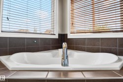 Built-in white soaking tub with a chrome faucet, surrounded by brown square tiling - 