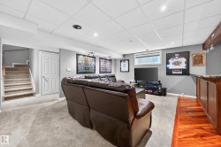 Finished lower level featuring carpeted flooring, a drop ceiling with recessed lighting, a built-in bar with wood-finish flooring, and a window providing natural light - 