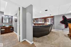 Lower-level recreation space featuring recessed lighting, a built-in wet bar with wood shelving, and durable carpet flooring - 