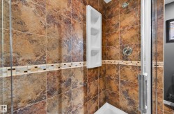 Shower enclosure featuring textured brown and tan tile, a decorative mosaic accent band, a built-in multi-shelf storage unit, and polished chrome fixtures - 