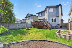 Expansive backyard featuring a manicured lawn, full privacy fencing, a multi-level wood deck with stairs, and a raised garden bed - 