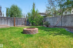 Expansive backyard featuring a central brick fire pit, manicured lawn, perimeter landscaping, and a wood privacy fence - 