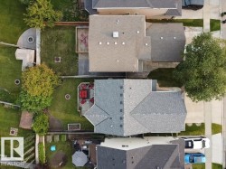 Expansive backyard featuring a curved concrete patio with a built-in fire pit, a wooden deck, and a manicured lawn - 