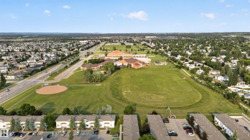 Expansive aerial panorama showcasing a residential community with abundant green spaces, including a large playing field and a baseball diamond - 33 Brookside Avenue, Spruce Grove, AB 